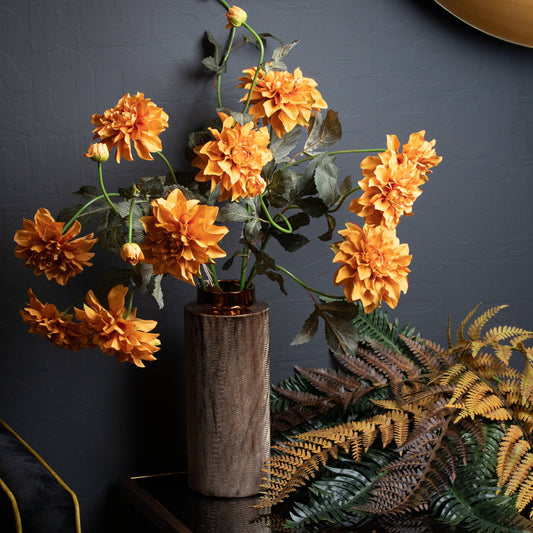 Artificial orange dahlia spray arranged in a tall rustic vase with realistic detail