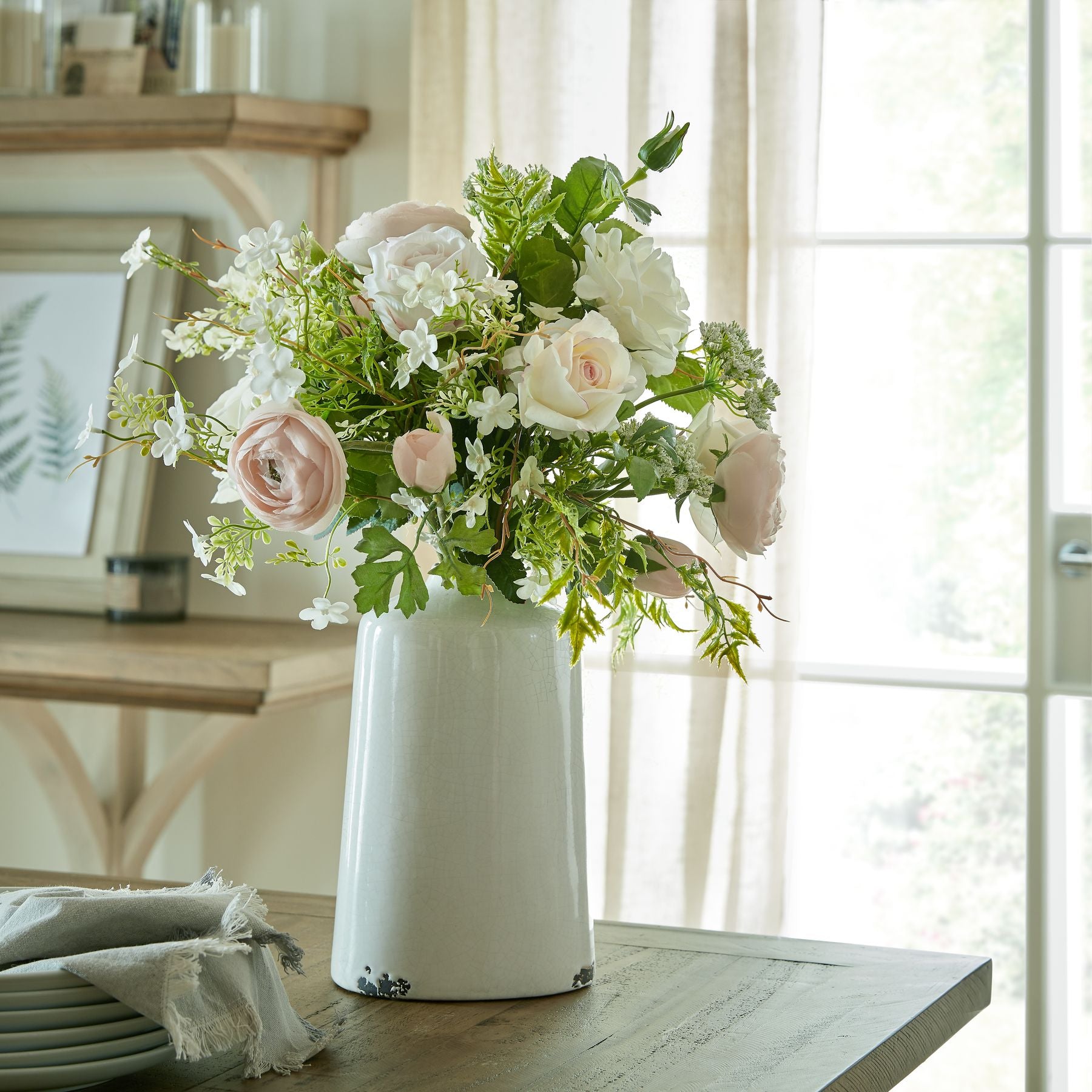 Pastel pink ranunculus bouquet styled in a white jug on a wooden table – a fresh and bright look for spring home styling.