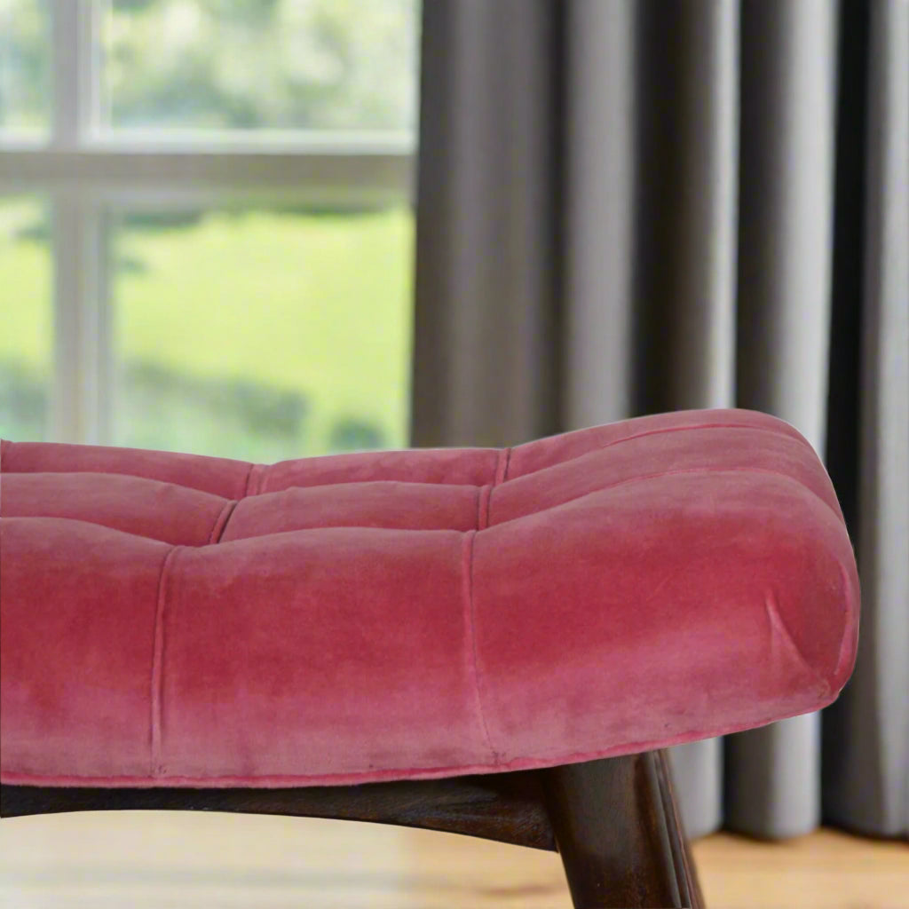 Close-up focus on the left edge of the upholstered pink velvet seat of the stool, with a partial view of its wooden legs.