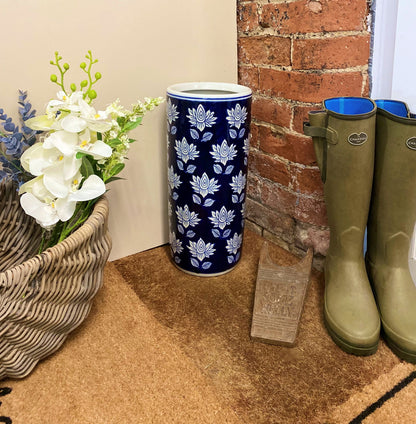 Purple Flamingo blue and white floral ceramic umbrella stand, styled in a hallway entrance with a wicker basket of flowers and green wellington boots.