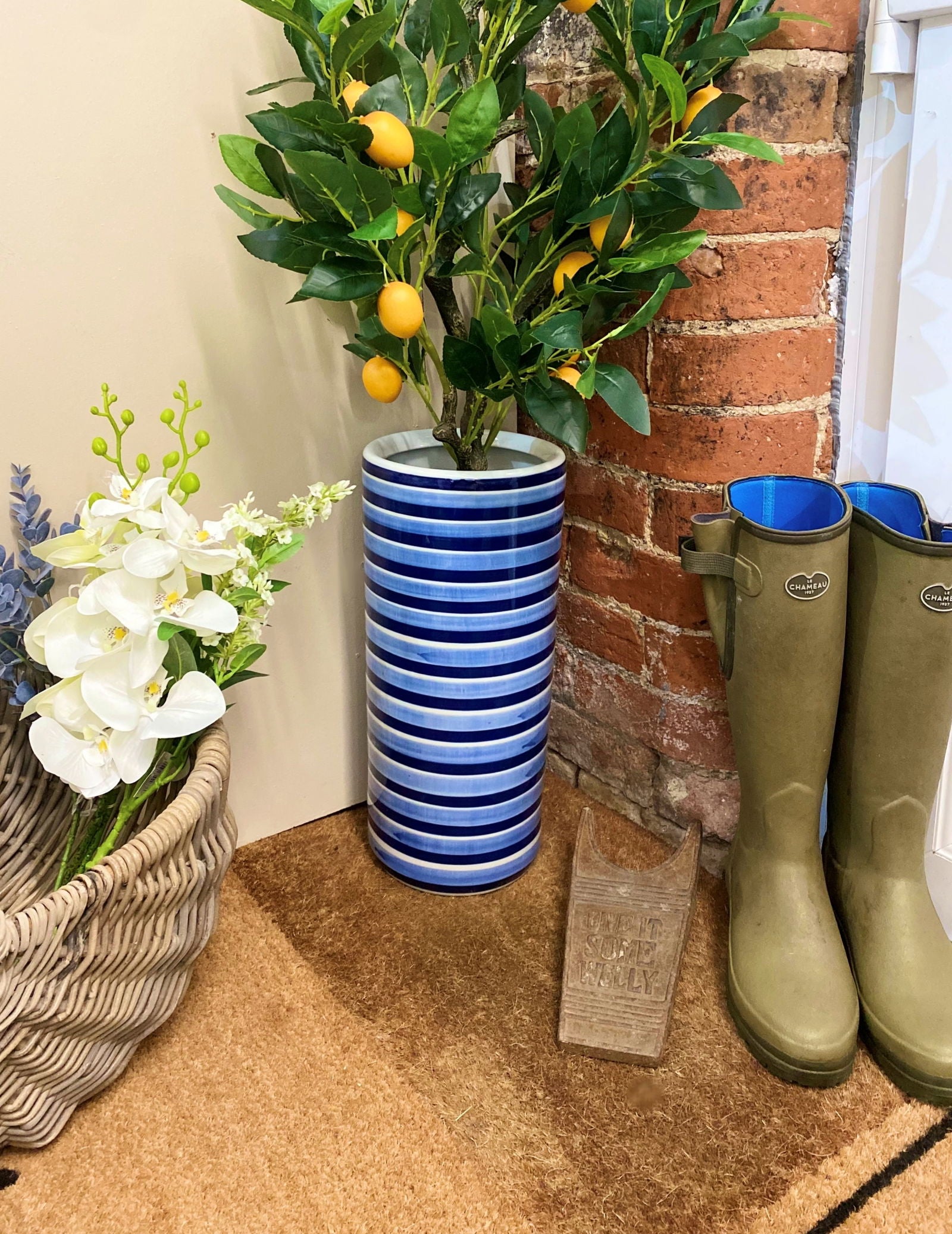 Purple Flamingo blue and white striped ceramic umbrella stand with a lemon tree plant, styled in a hallway entrance with wellington boots.