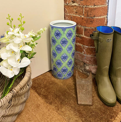 Purple Flamingo green and blue diamond print ceramic umbrella stand providing stylish storage in a hallway, next to a wicker basket and boots.