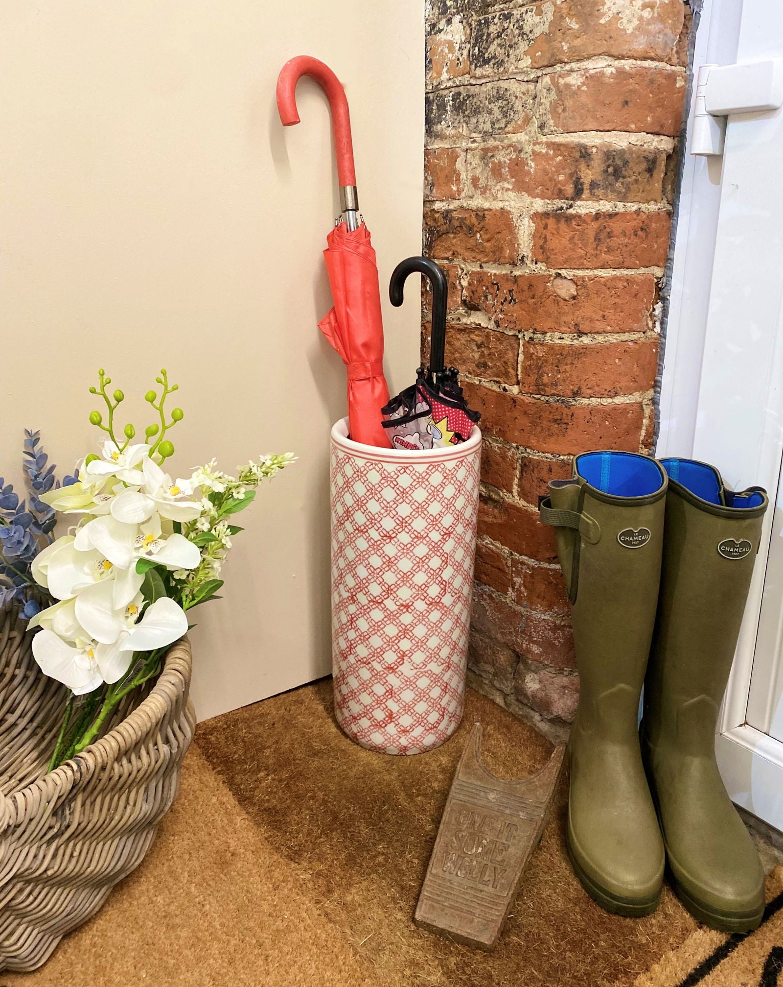 Purple Flamingo red and white daisy chain ceramic umbrella stand holding two umbrellas, perfect for a tidy hallway.