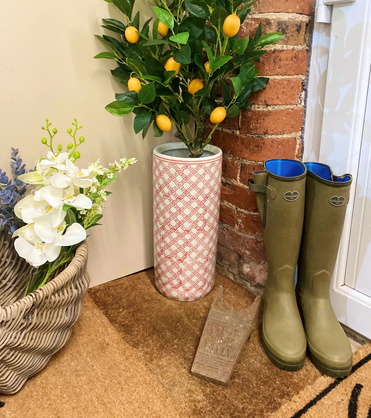 Purple Flamingo red and white daisy chain ceramic umbrella stand with a lemon tree plant, styled in a hallway entrance with wellington boots.