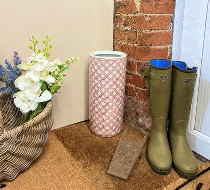 Purple Flamingo red and white daisy chain ceramic umbrella stand providing stylish storage in a hallway, next to a wicker basket and boots.