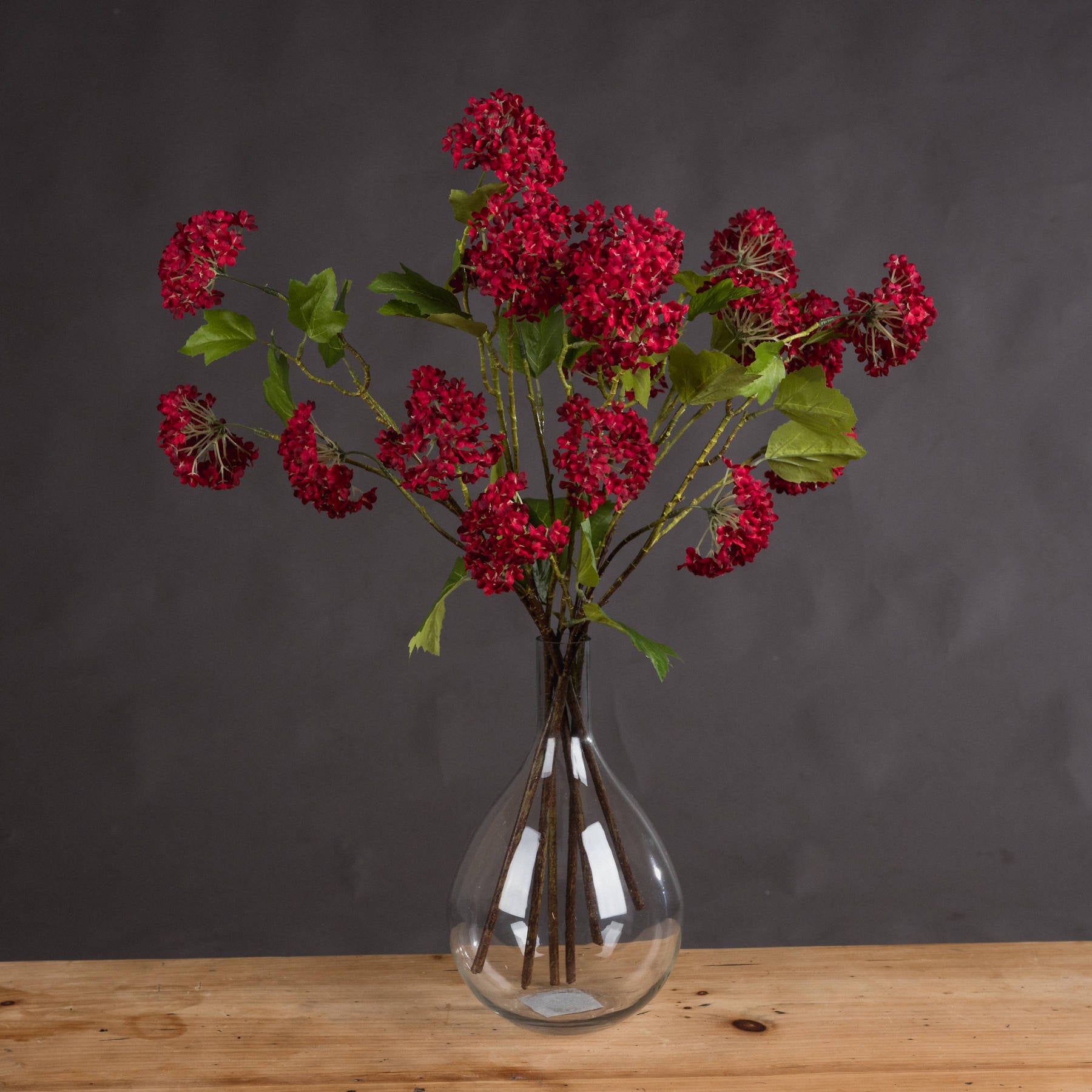 Bunch of red autumnal viburnum stems in a clear vase on a wooden surface.