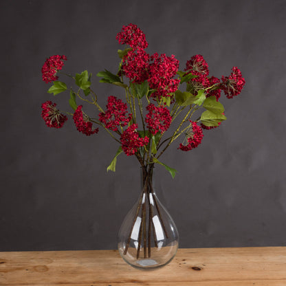 Bunch of red autumnal viburnum stems in a clear vase on a wooden surface.