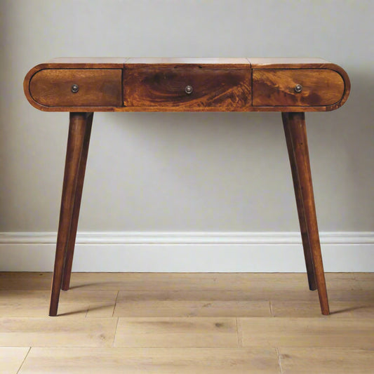 Front view of the rounded dressing table, with chestnut finish, displaying nordic style legs and three drawers.