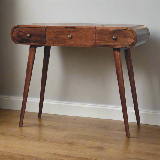 Angled view of the rounded dressing table with honey caramel finish showing Nordic legs and closed drawers.