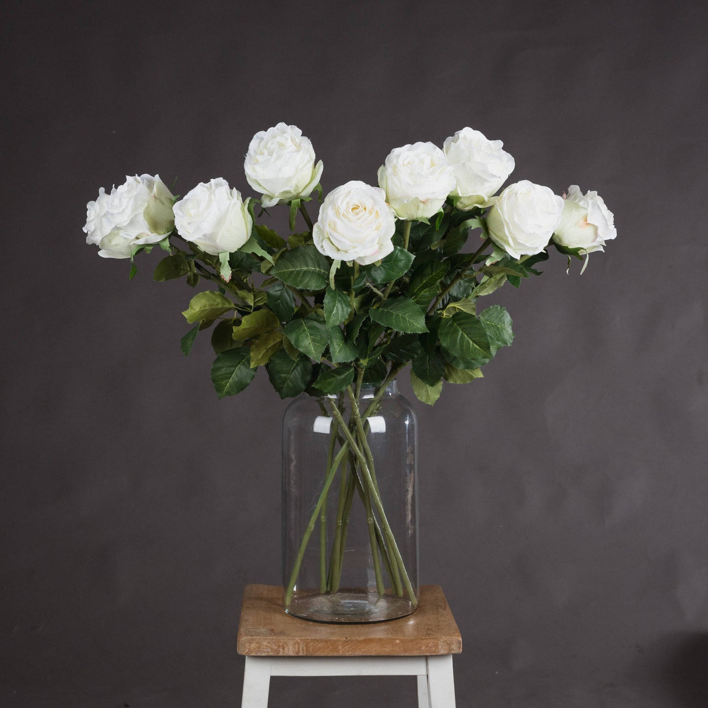 A bunch of traditional white roses in a clear vase on a wooden stool.
