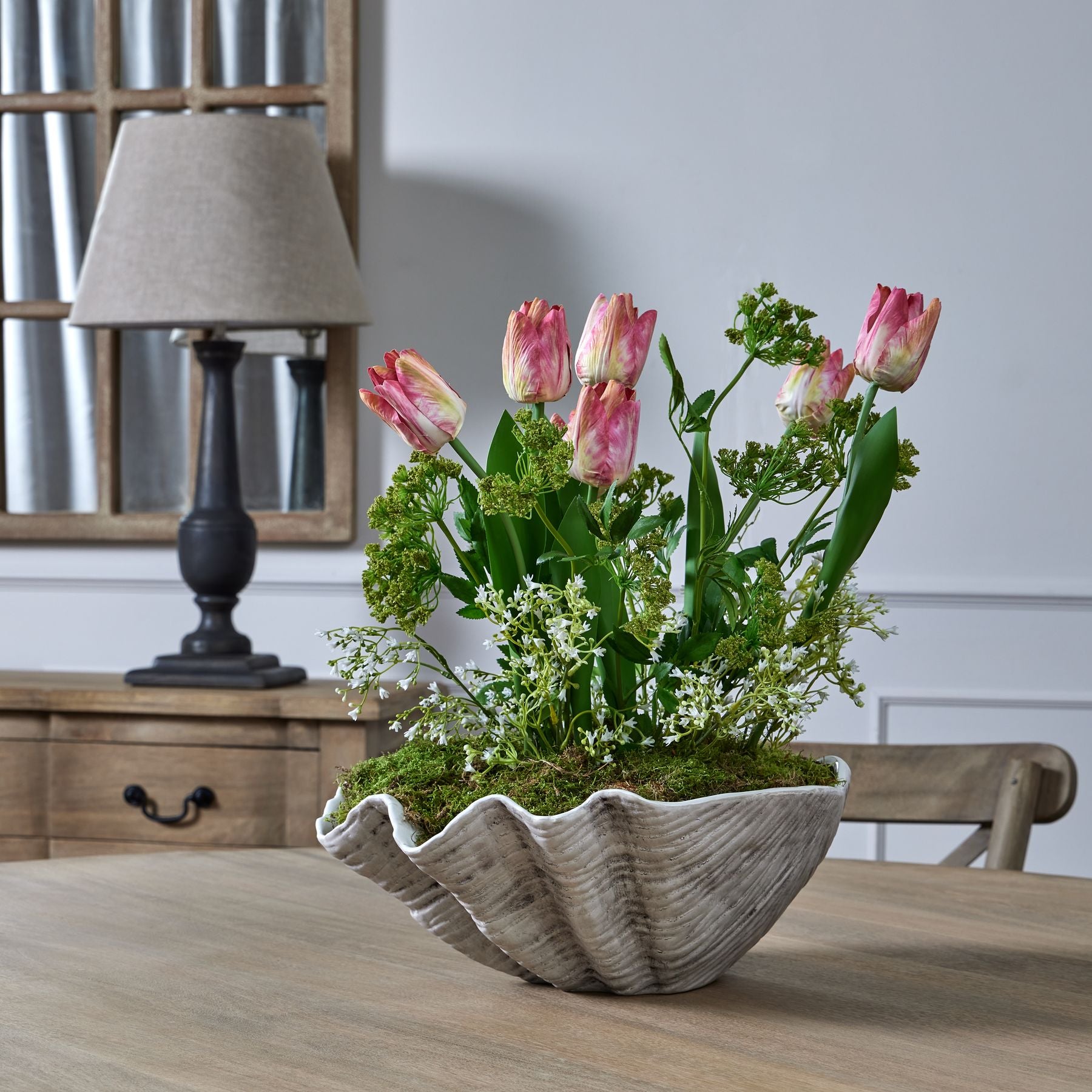 White Gypsophila and pink tulips styled in a decorative shell pot on a dining table. For spring or summer styling, from Purple Flamingo.