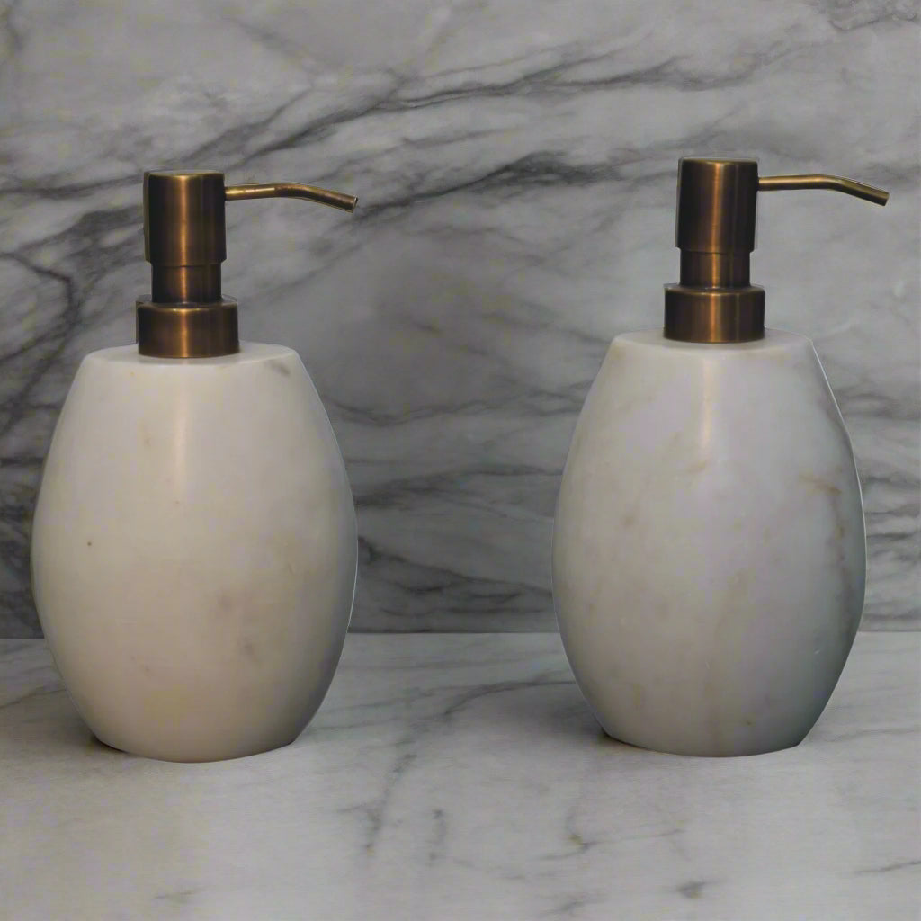 Front view of the two white marble dispensers from the set, placed on a cream-colored surface.