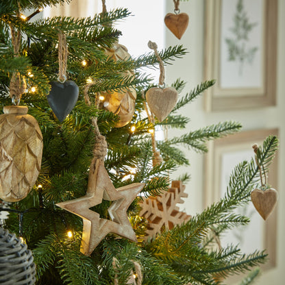 A white wash small wooden hanging star decoration hanging on a green Christmas tree with lights, showcasing its festive appeal.