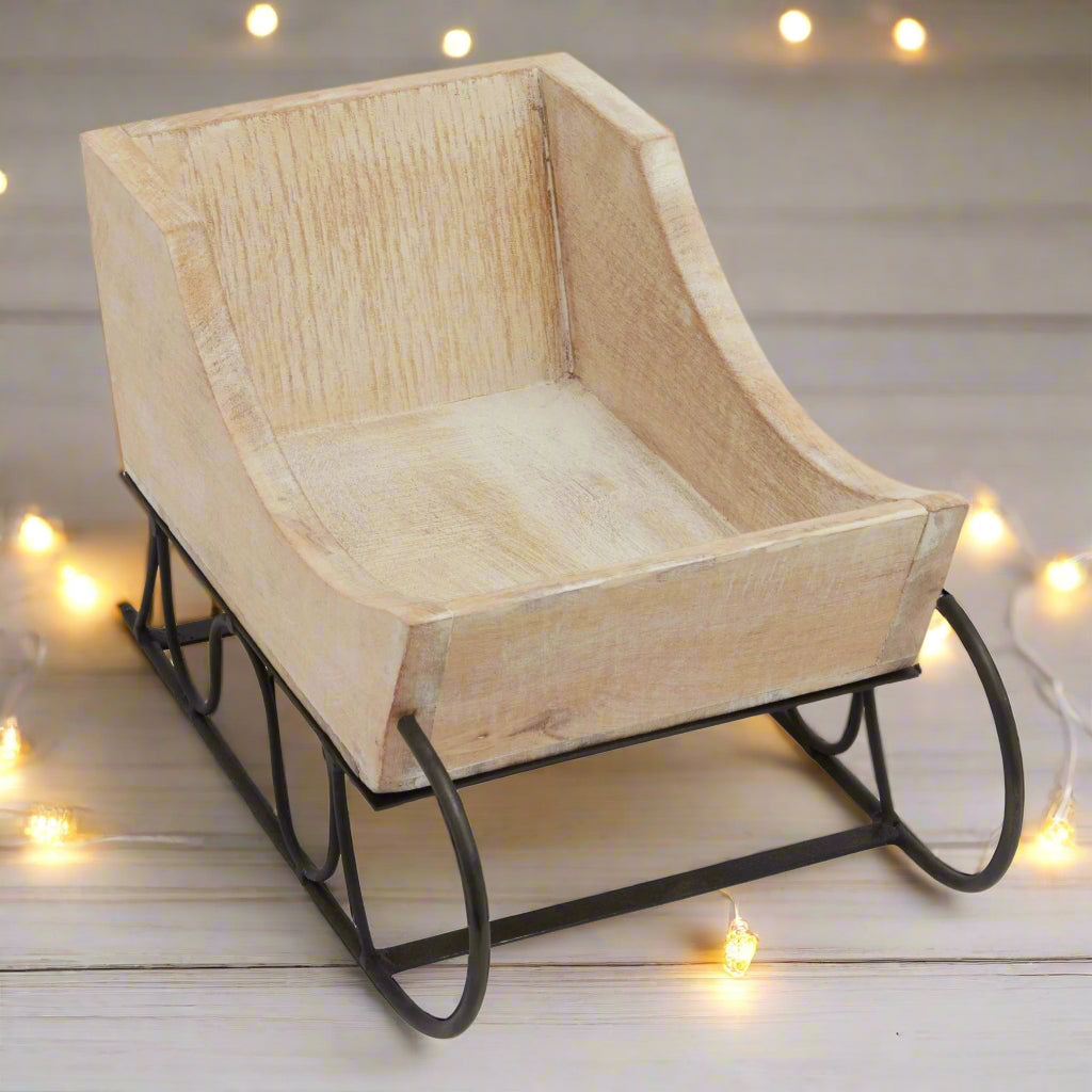 Angled view of a whitewash wooden decorative sleigh, highlighting its intricate woodwork and rustic elegant design for festive displays.