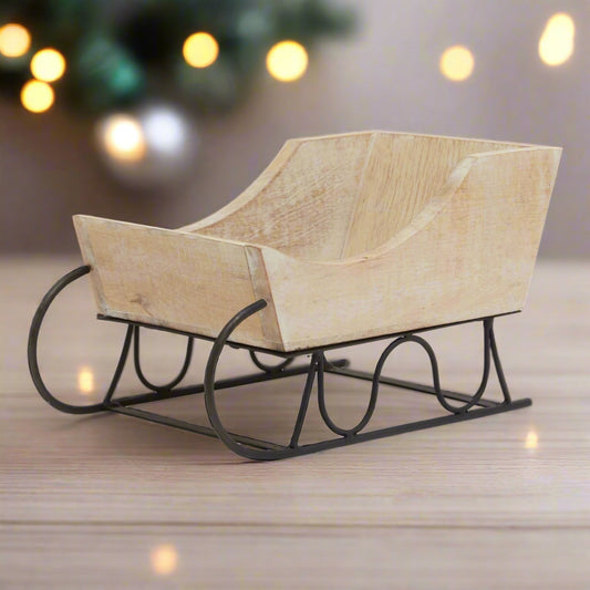 A charming white wash wooden decorative sleigh with a distressed finish and black metal runners, perfect for rustic or Scandinavian festive home decor.
