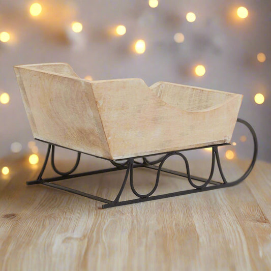 Side view of a whitewash wooden decorative sleigh, showing the distressed wood texture and curved black metal runners.