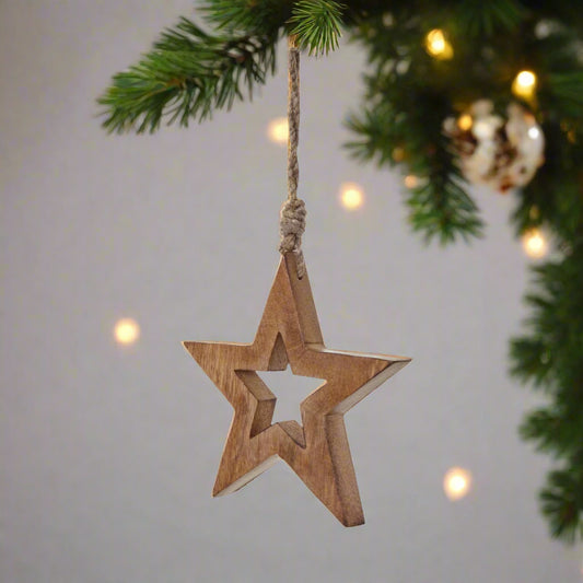 Wooden star shaped decoration with cut-out star middle hanging by the attached twine from a Christmas tree with fairy lights.