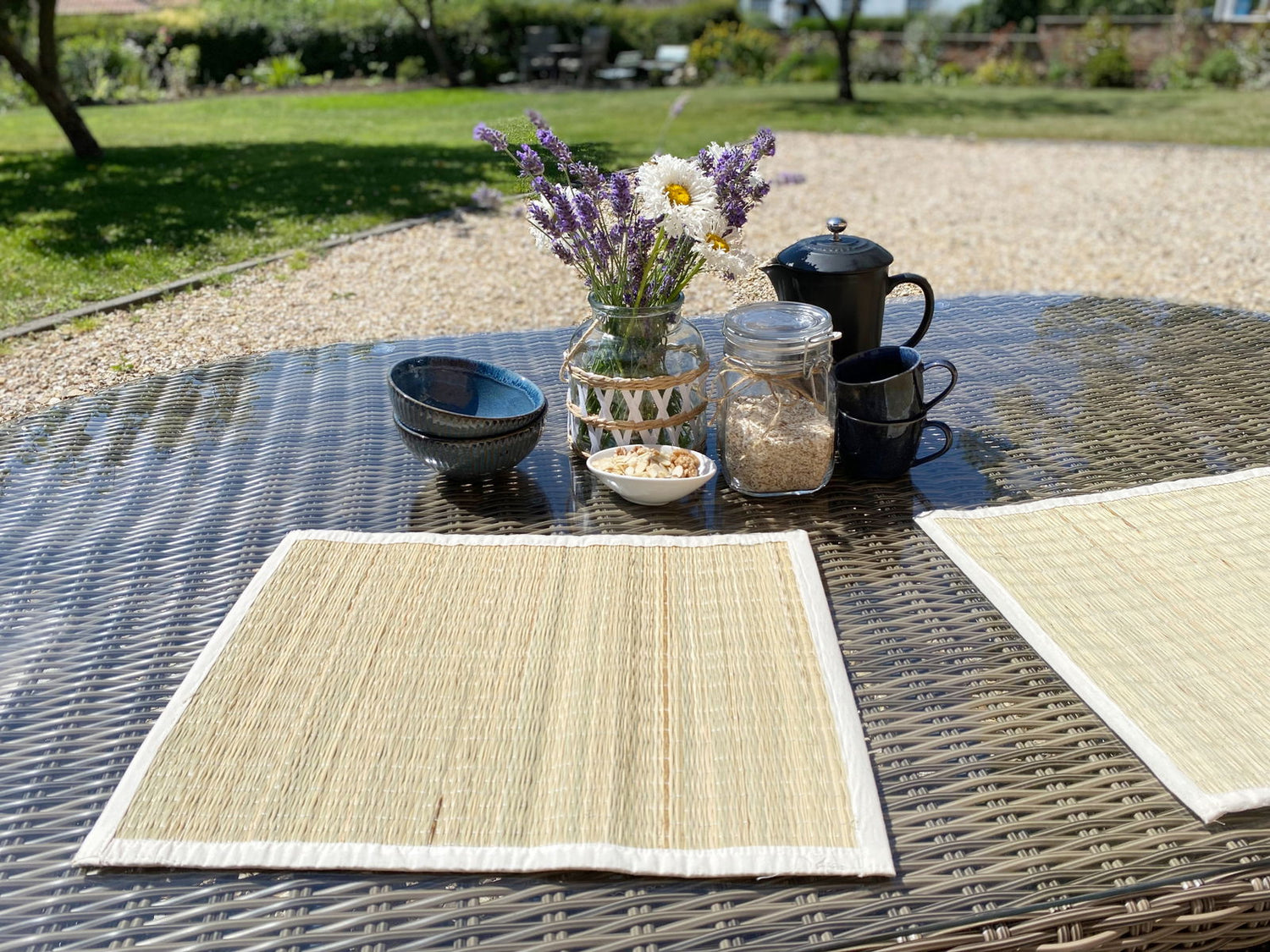 Natural woven grass jute place mats styled on an outdoor dining table with rustic crockery and flowers, offering an earthy and elegant dining setup.